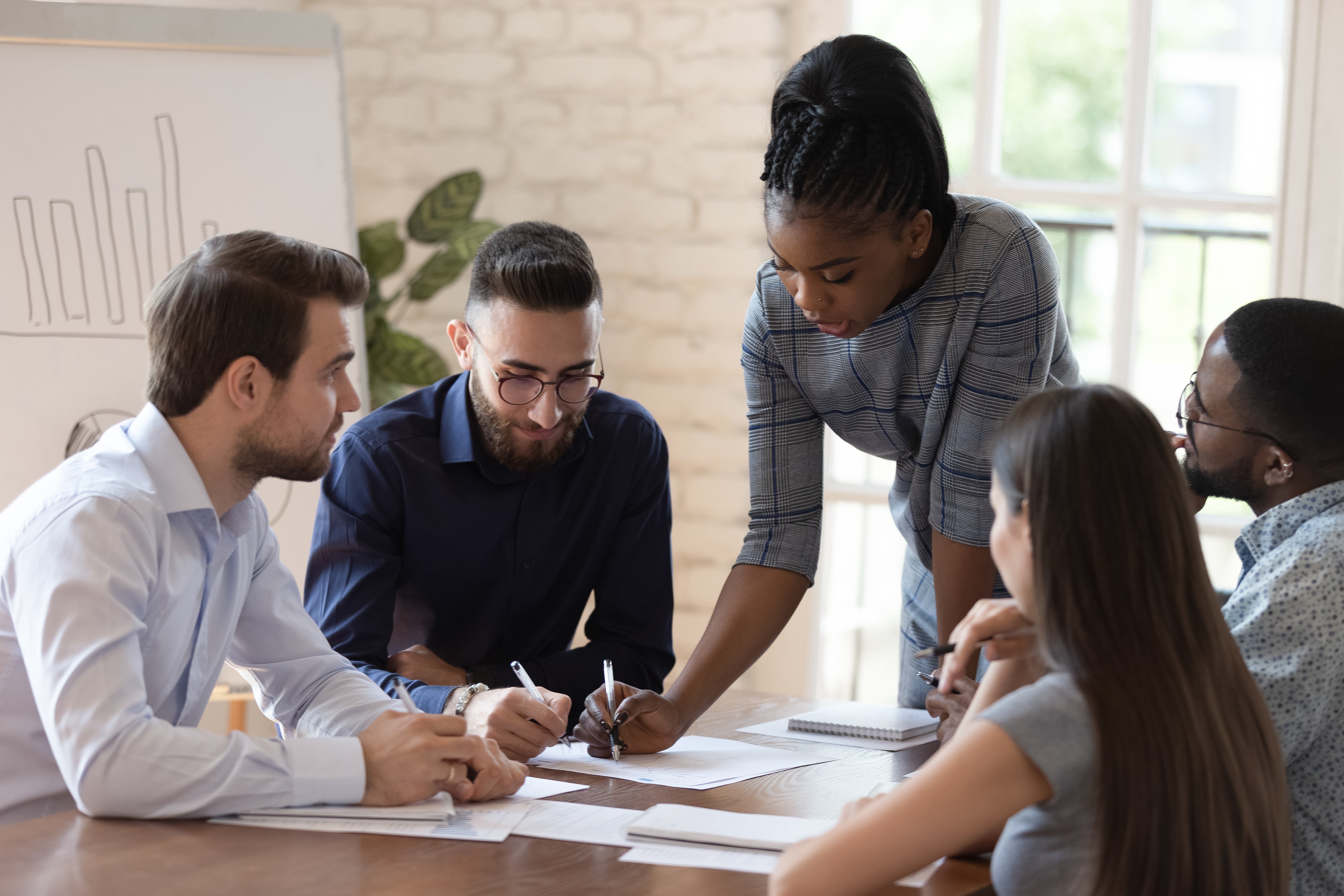 Procurement executive stands at conference table explaining spend analysis reports to four members of procurement team.