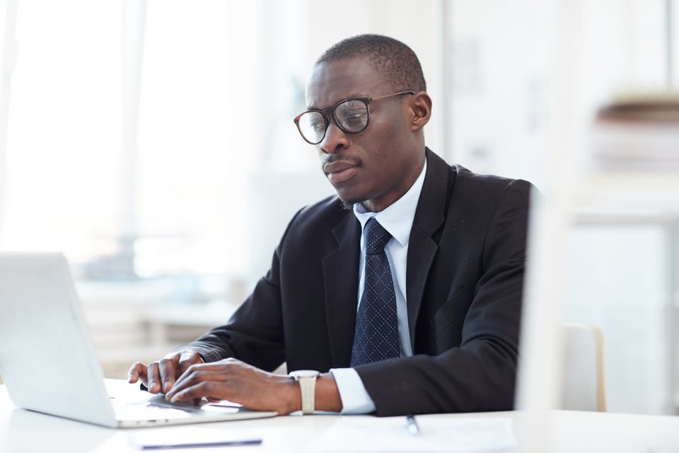 Procurement manager at desk reviews spend analysis on laptop computer, looking concerned about inflation impact on supply chain.