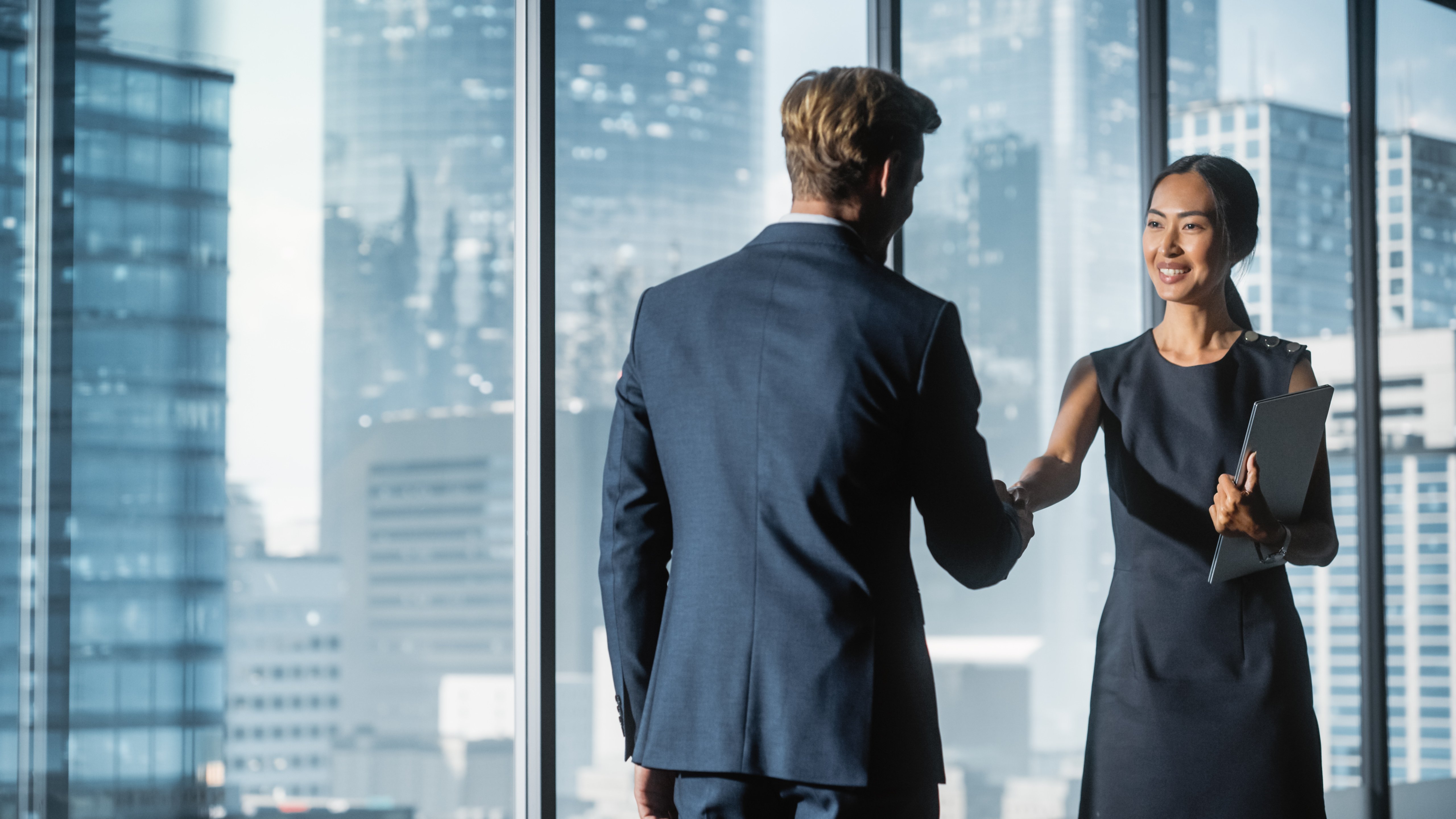 Procurement specialist shakes hands with his supplier’s representative in high-rise office building