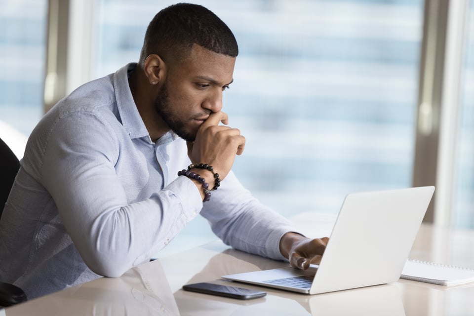 Procurement manager sits alone at conference table, reviewing procurement analytics on his laptop computer.