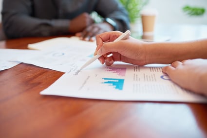 Female business owner reviews supplier diversity spend report with pen, while Black executive sits on other side of table. 