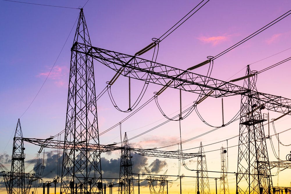 High-voltage power lines at sunset symbolizing increased grid demand and rising electricity costs for commercial and industrial businesses.