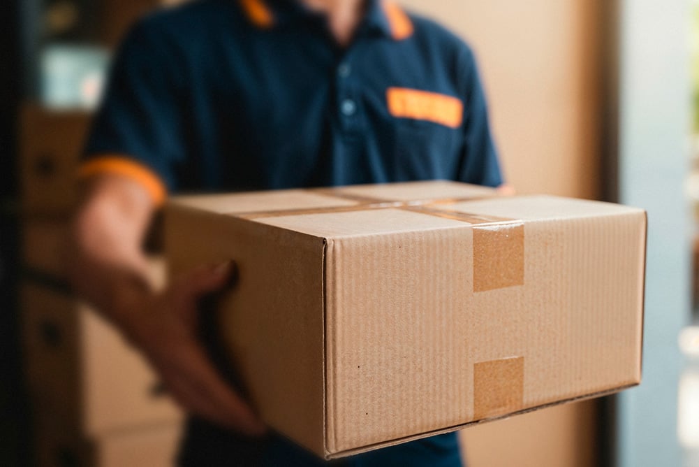 Close-up of a delivery worker holding a cardboard shipping box, representing business shipping costs, logistics efficiency, and the importance of managing carrier contracts to prevent overpayment on shipping.